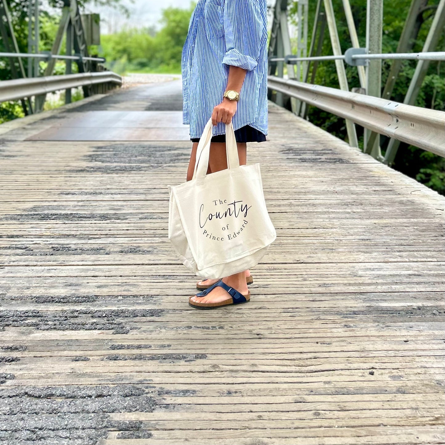 Person holding canvas market tote bag standing on a bridge.
