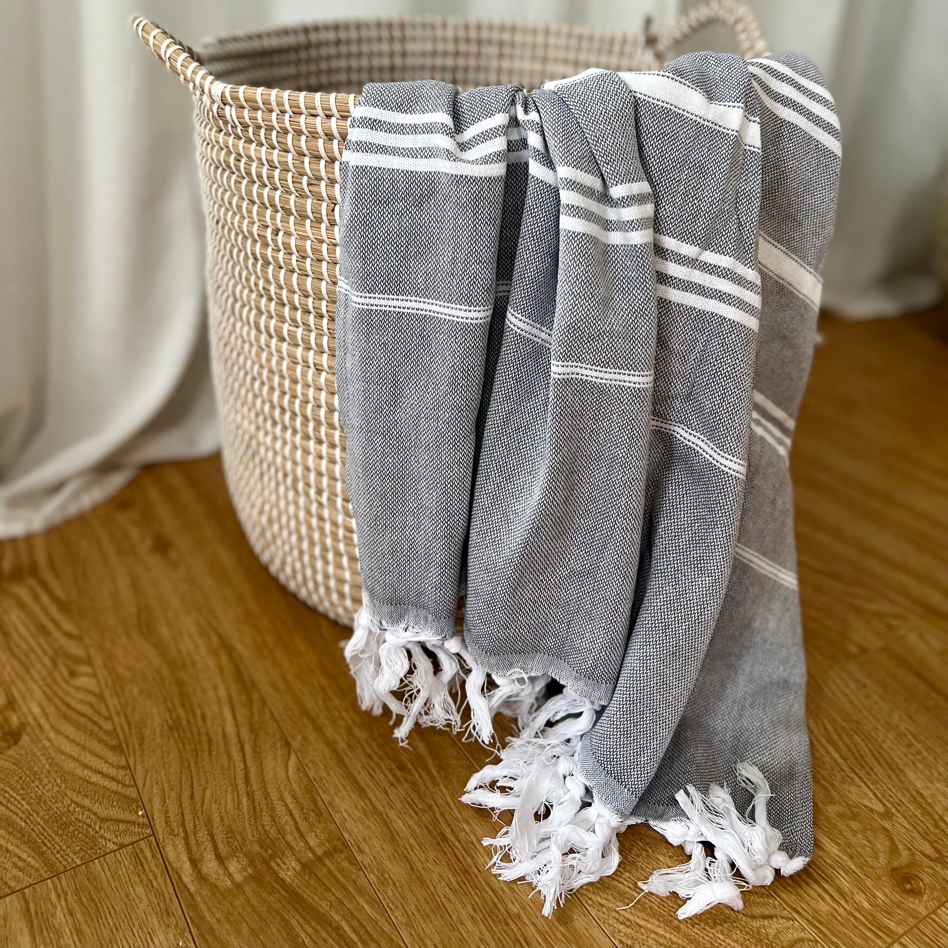 A grey with white stripes Turkish towel draped over a wicker basket.